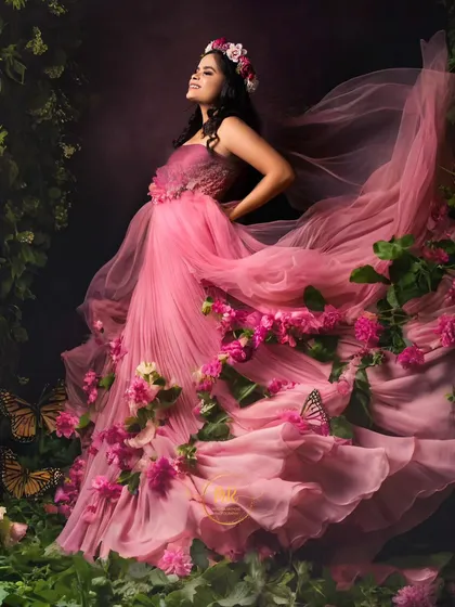 A fairytale moment brought to life. This fine art pregnancy portrait features a flowing pink gown adorned with flowers and butterflies, creating a magical, enchanted forest theme right in the studio.