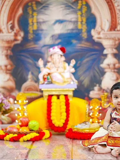 A calm and composed portrait of a baby girl sitting patiently in our colorful and detailed Ganpati celebration setup.