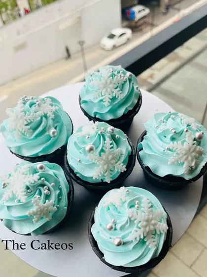 These Frozen-themed cupcakes are a popular choice for kids' parties. Each eggless chocolate cupcake is topped with light blue cream, edible silver pearls, and a delicate, handcrafted snowflake, perfect for a winter wonderland celebration.