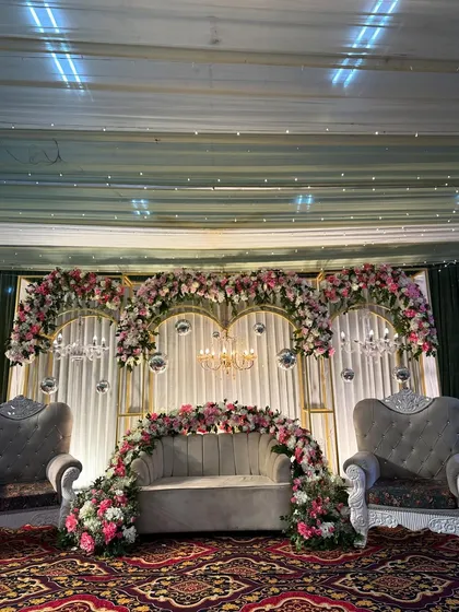 A glamorous stage for an engagement party. The backdrop combines golden arches, white drapery, sparkling disco balls, and elegant chandeliers, all framed by lush garlands of pink and white flowers for a truly celebratory feel.