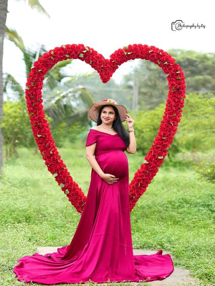 Framed by love. This striking portrait features our large, red floral heart prop, perfectly framing the mother-to-be in her beautiful magenta off-shoulder gown.