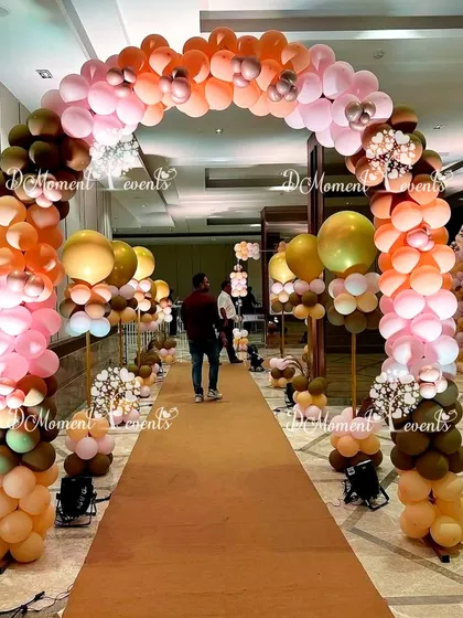 A long walkway decorated with boho-themed balloon arches. The path is lined with balloon pillars in shades of brown, peach, and pink, creating an impressive entrance experience.
