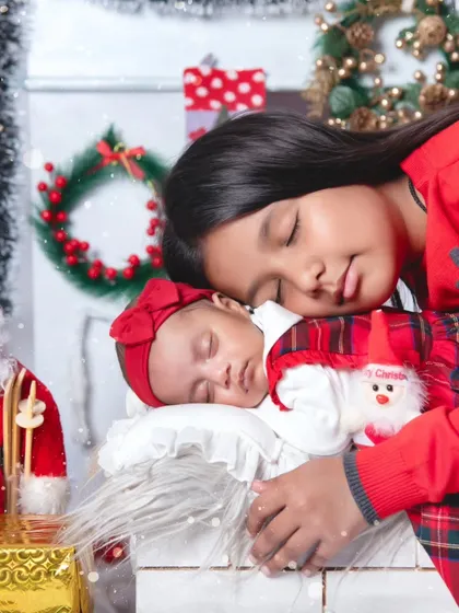 There's nothing more special than the bond between siblings. Here, an older sister gently cuddles her sleeping newborn sister in a festive Christmas-themed setup, creating a memory the family will cherish forever.