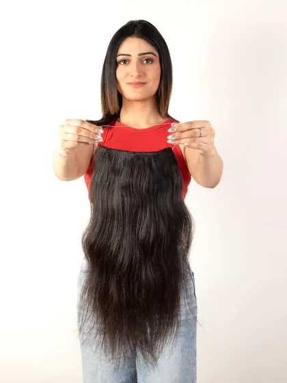 A model holding a weft of hair extensions, showing the full length and texture.