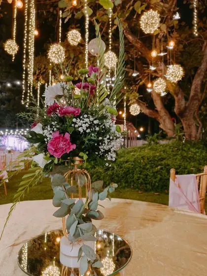 The magic is in the details. This close-up shows an elegant floral centerpiece on a mirrored tabletop, reflecting the warm glow of hanging fairy light orbs that create a dreamy, romantic ambiance for an evening event.
