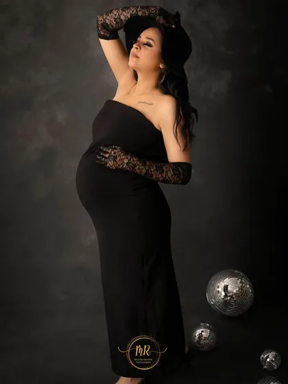 A playful and stylish pose in a black strapless dress. The mother-to-be wears a hat and lace gloves, with disco balls on the floor adding a fun, celebratory element.
