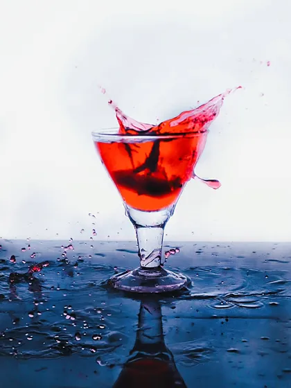 A dramatic splash of red liquid in a cocktail glass, frozen in time to create a sense of excitement and motion for a beverage brand.
