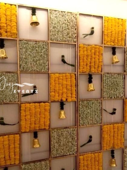 A creative checkerboard backdrop featuring alternating squares of marigolds, green fillers, hanging bells, and parrot motifs. This design adds a unique and festive touch to any half saree ceremony.