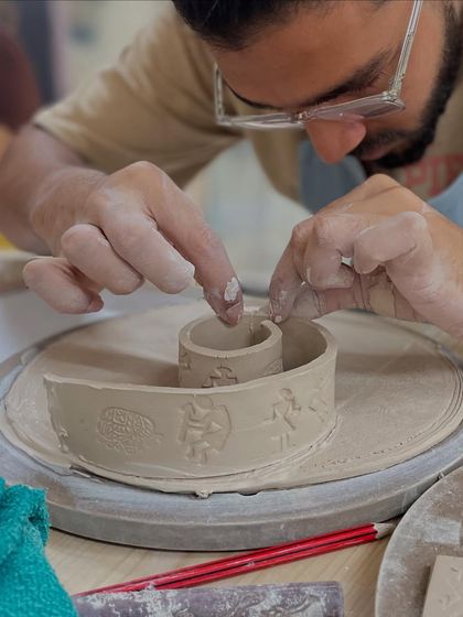 A student carefully constructs a piece using stamped slabs of clay, showing the precision that hand-building allows.