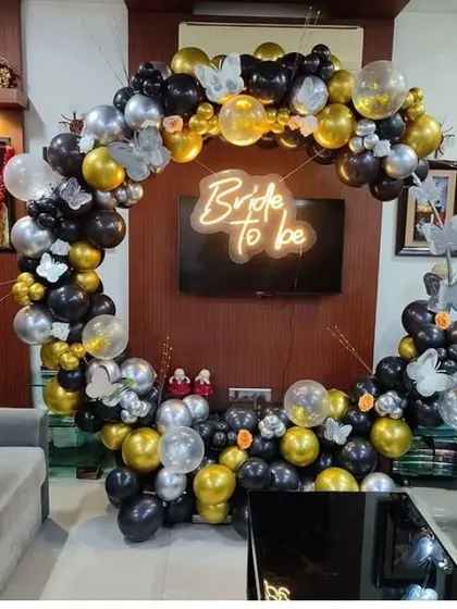 A 'Bride to be' living room setup with a circular balloon arch in black, gold, and silver, accented with butterflies.