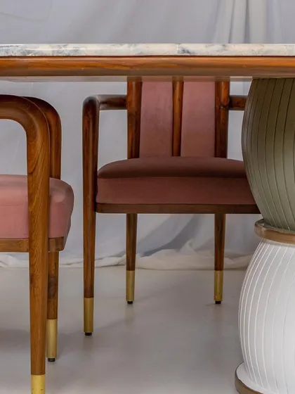 A detail shot of the 'Damru' dining table and 'Svelte' chairs, showcasing the blend of wood, brass, and PU materials.