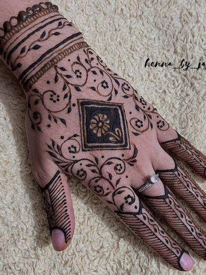 A unique design featuring a square motif with a flower inside, surrounded by swirling vines. The fingers have simple line work, creating a modern look.