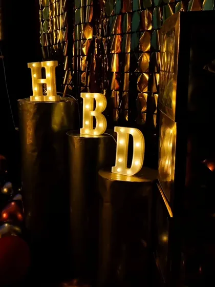 Marquee letters are a great way to personalize your event. Here, 'HBD' letters are displayed on pedestals against a gold sequin wall, adding a touch of glamour to the birthday decor.