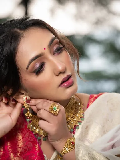 The model adjusting her earring, a classic pose that draws attention to the beautiful gold jewelry.