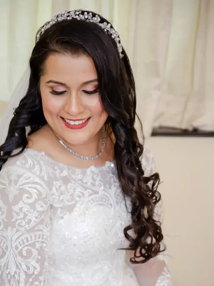 A beautiful close-up of the bride's finished look. Her hair is styled in voluminous curls, and her makeup features a soft pink eyeshadow and a matching lip color.