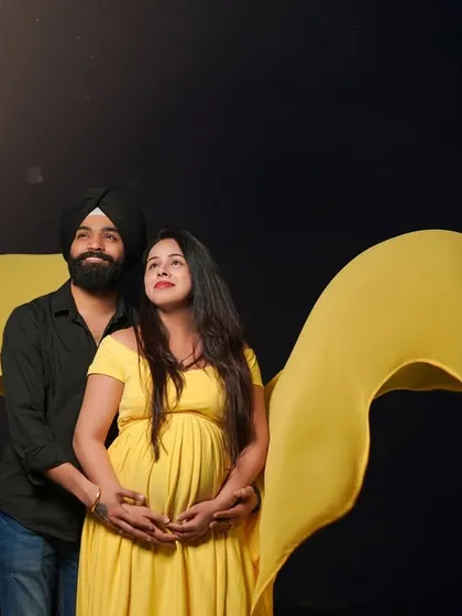 A creative and striking studio portrait of an expecting couple. The flowing yellow fabric creates a beautiful wave of color against the dark backdrop, symbolizing the bright future ahead.