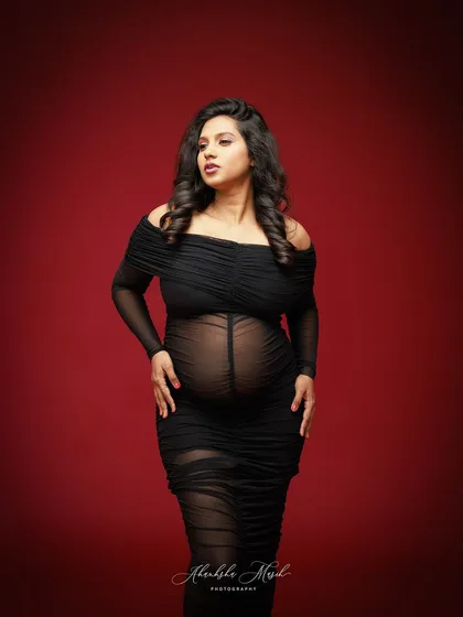 A powerful and classic portrait. The sheer black gown against a rich red backdrop highlights the beautiful silhouette of the baby bump, capturing the strength and allure of expectancy.