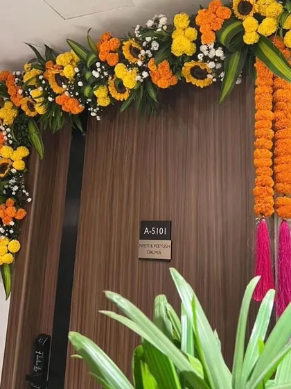 A traditional and auspicious floral decoration for a housewarming, with marigold and sunflower garlands framing the apartment door.