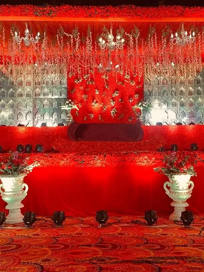 A magnificent all-red wedding stage, featuring a textured floral backdrop, hanging chandeliers, and classic white urns.