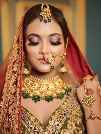 A beautiful bridal look with a green and red lehenga. The makeup features a classic smokey eye and a nude lip.