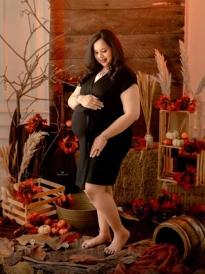 A rustic, autumn-themed portrait with warm, moody lighting. The rich reds and oranges of the set create a cozy and artistic atmosphere for this beautiful maternity shot.