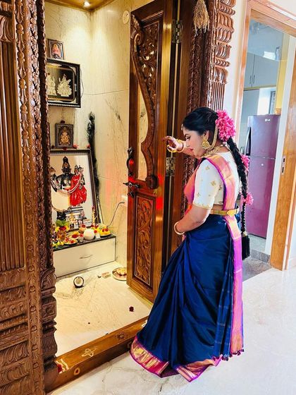 A candid moment by the pooja room. The traditional braid adorned with fresh pink flowers is a key element of this classic South Indian ceremony look.