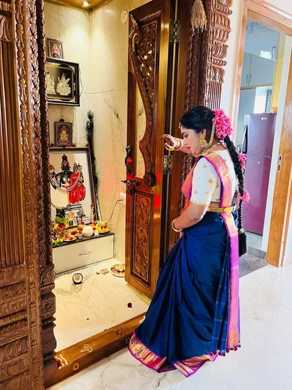 A candid moment of the bride by the pooja room before her bangle ceremony. The traditional hairstyle with fresh flowers adds a beautiful touch.