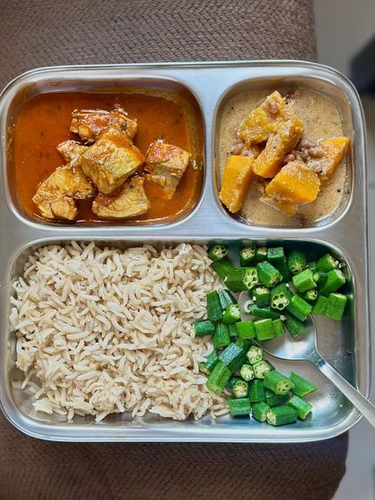 This plate combines brown rice with fish curry, pumpkin dal, and steamed okra, offering a mix of protein and fiber.