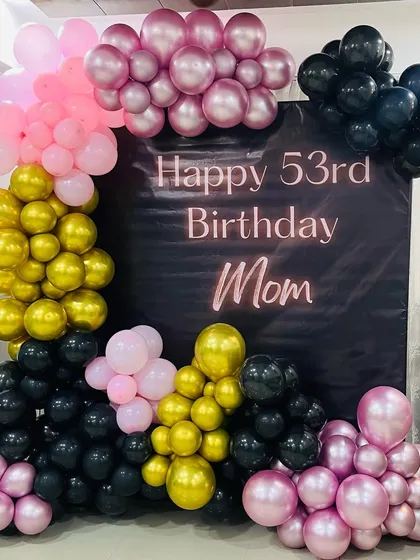 A heartfelt 53rd birthday surprise for Mom. This decoration uses a custom backdrop with a personal message, framed by an elegant balloon arrangement in pink, black, and gold.