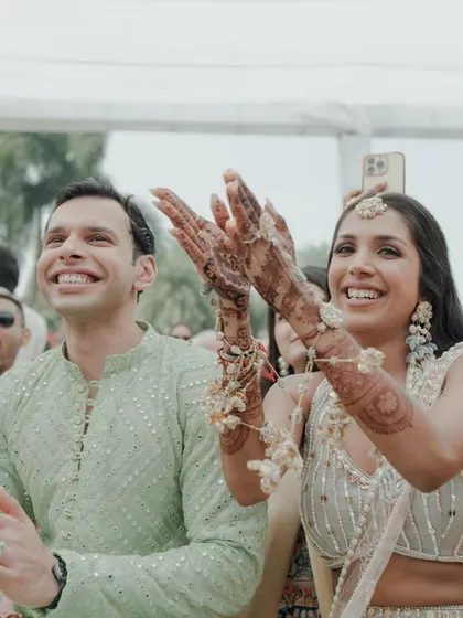 The couple clapping and cheering during their Haldi ceremony, fully immersed in the joy of the celebration.