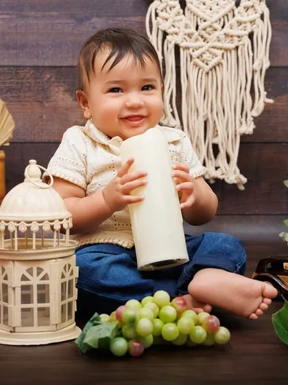 A happy one-year-old boy plays with a lantern and grapes in a cozy, rustic-themed setting.