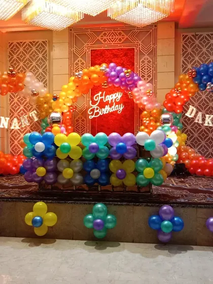 A colorful double balloon ring setup on a stage. This decoration uses bright, rainbow-colored balloons and flower-shaped clusters to create a fun and festive look for a joint birthday party.