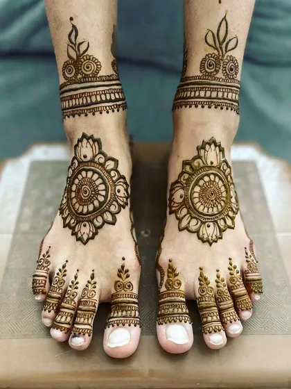 A simple and elegant foot mehandi, featuring a floral mandala on the top of the foot and matching minimal bands on the toes and ankle.