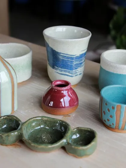 A colorful group of cups, bowls, and a small pitcher, showcasing various glazing techniques like stripes and dipping.