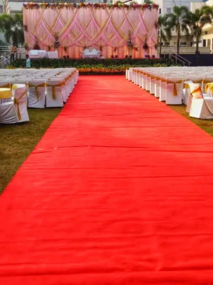 For large gatherings, I manage the complete seating layout and decor. This image shows a long red carpet aisle leading to the main stage, with formal, covered chairs arranged theater-style to accommodate a large number of guests.
