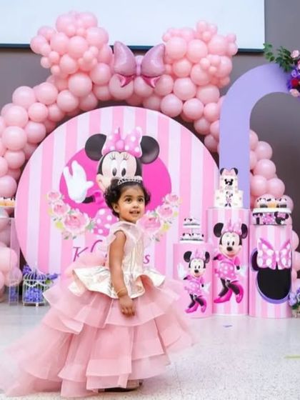 A dreamy Minnie Mouse theme for a little girl's birthday. This setup includes custom-arched backdrops, a large balloon bow, and character prints, all in a lovely pink and purple color scheme.