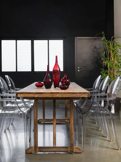 Where industrial meets elegance. This 1200 sq. ft. fashion showroom in Mumbai tells a story of contrasts, with a rustic wooden table and modern transparent chairs set against a dramatic black wall.
