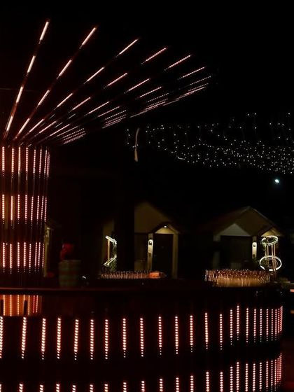 A dramatic, modern bar structure with radiating LED lights, creating a central glowing tree-like feature for a Sangeet under the stars.