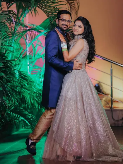 A full length portrait of the couple, showcasing their elegant engagement outfits. The groom's royal blue sherwani complements the bride's shimmering gown perfectly.