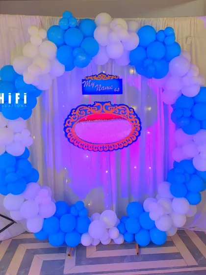 A simple and elegant naming ceremony backdrop with a blue and white balloon circle and a customizable nameplate.