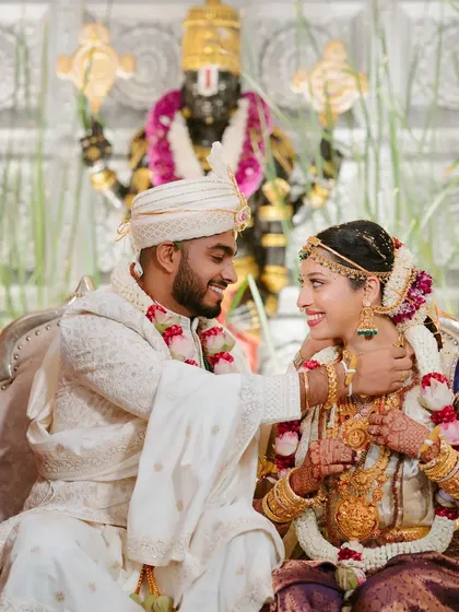 A beautiful moment from a traditional Hindu wedding. The backdrop features a serene depiction of Lord Venkateswara, framed by fresh greenery, adding a divine touch to the ceremony decor.