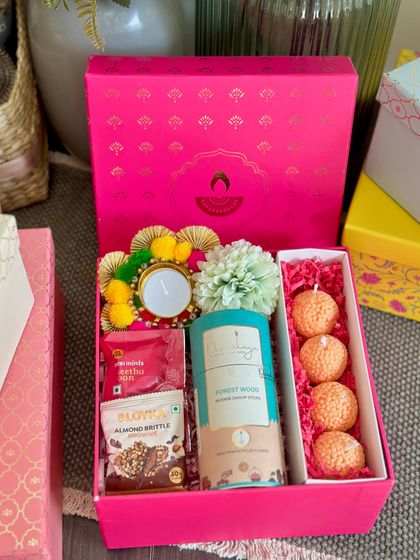 This vibrant pink Diwali box is all about festive fun. It contains a set of four ladoo-shaped candles, dhoop sticks, almond brittle, and a decorated tealight holder, making it a colorful and joyful gift.