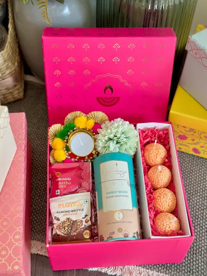 This vibrant pink Diwali box is all about festive fun. It contains a set of four ladoo-shaped candles, dhoop sticks, almond brittle, and a decorated tealight holder, making it a colorful and joyful gift.