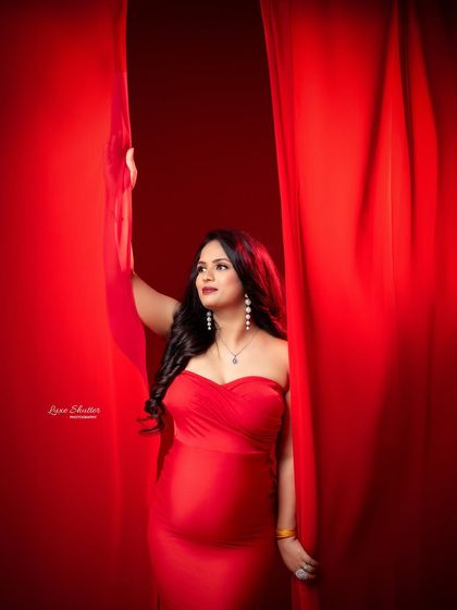 Carrying love in the boldest color. This mom-to-be peeks through dramatic red curtains, creating a sense of anticipation and theatrical beauty.