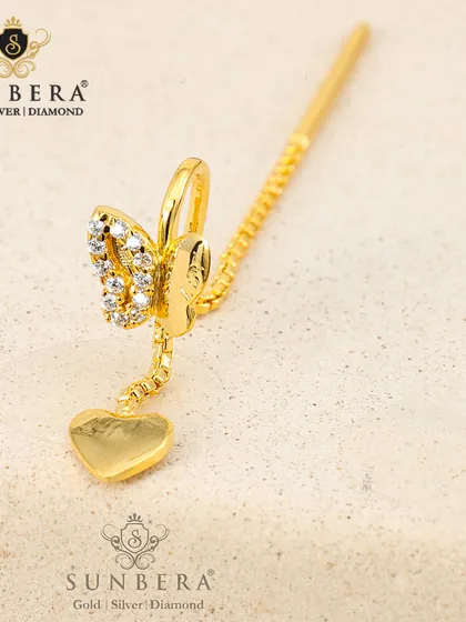 A unique gold ear accessory combining a butterfly stud with a delicate heart charm on a chain. This piece is designed to be worn as an ear cuff or climber, offering a trendy and playful look.