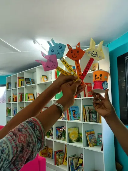 A group of children raise their handmade bunny puppets high. The collective energy and pride in their work is a beautiful sight, showing the power of creating together.