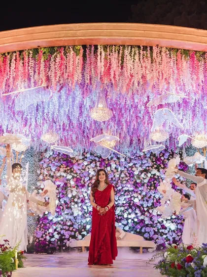 A fairytale reception in Ooty. The bride made a stunning entrance in a red gown, surrounded by dancers and a magical backdrop of hanging wisteria and a floral wall.
