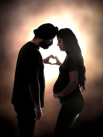 A creative silhouette of a couple forming a heart with their hands over the baby bump. This artistic shot uses backlighting to create a warm glow and a deeply symbolic image of their love.