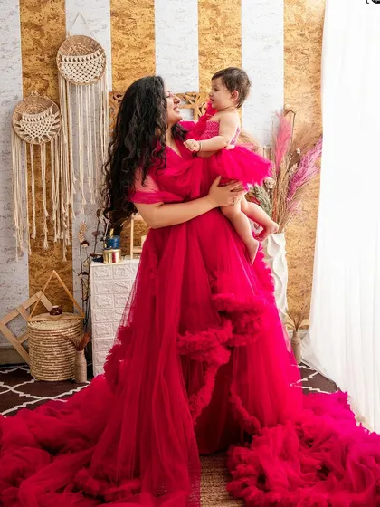 A mother lifts her daughter, both laughing and enjoying their special photoshoot together. The flowing red dress adds a touch of magic.