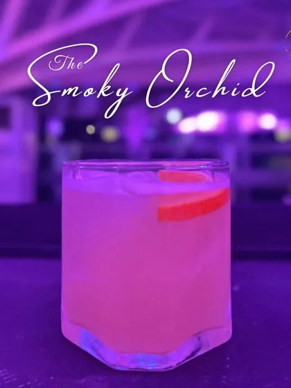 'The Smoky Orchid', a beautifully crafted cocktail with a soft pink hue, served over ice in a modern, angular glass. Its name hints at a complex and aromatic flavor profile.